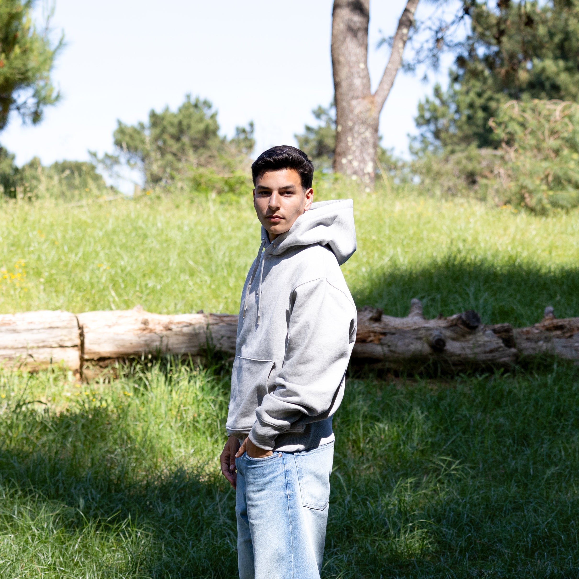 Mandelig model i grå hoodie i sidelæns frontvisning – hætten nede og lavet i 100% økologisk bomuld